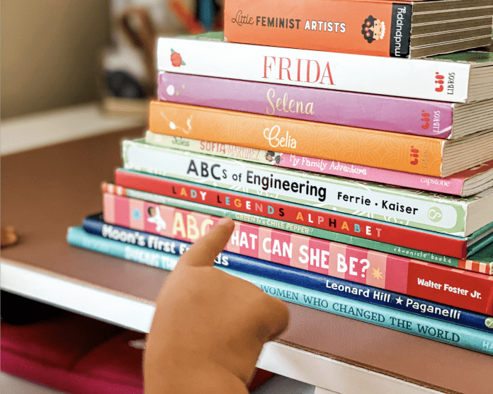 Toddler hand pointing at stack of children's books | Representation in Children's Books